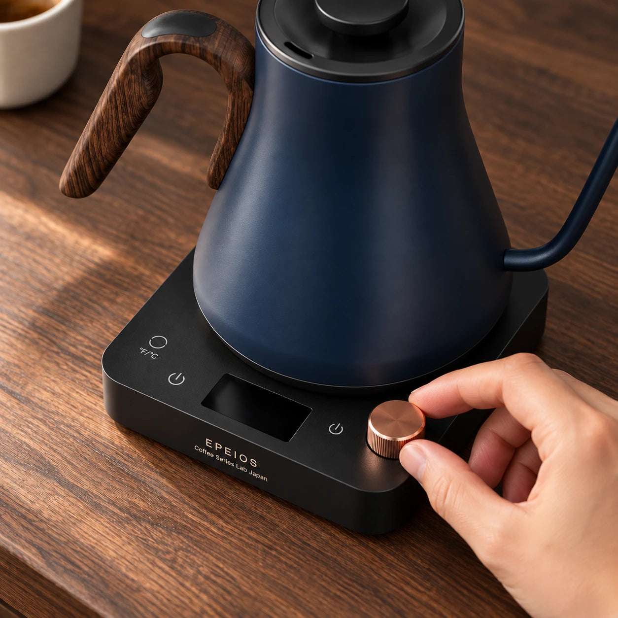A hand adjusting the copper temperature dial on the Navy Blue EPEIOS kettle base