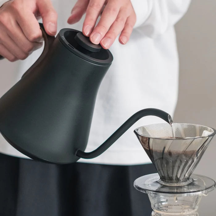 A black gooseneck kettle pouring into a glass coffee dripper