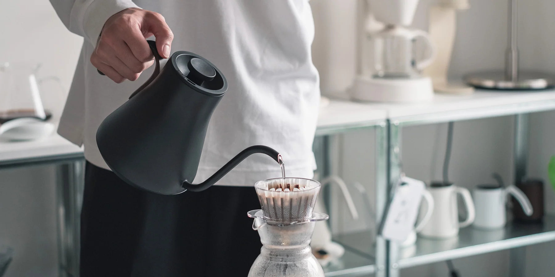 A barista pouring coffee with a black EPEIOS kettle in a bright coffee corner